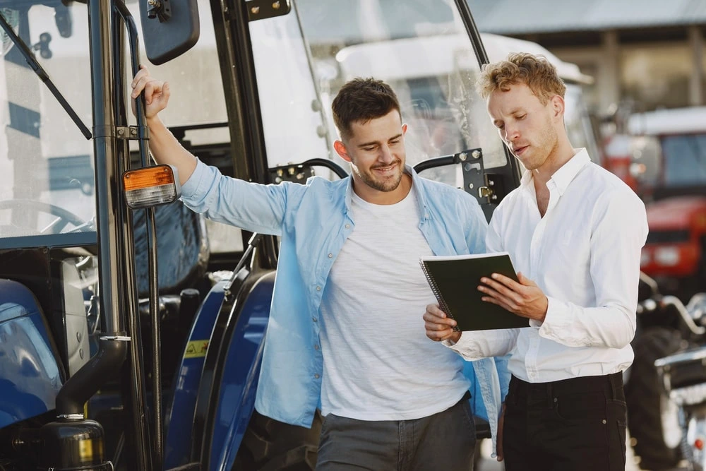 Business person stadning with notebook next to tractor