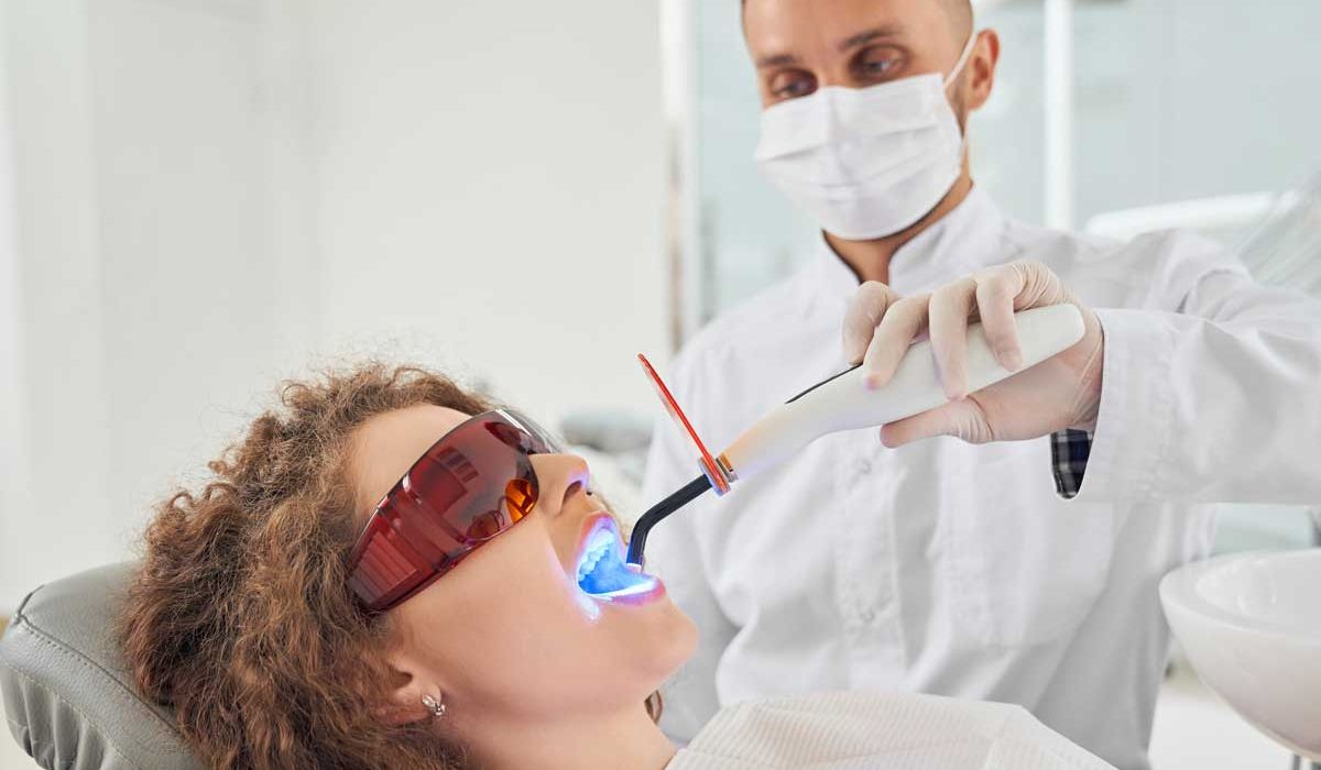 A woman wearing blue glasses and a red glove is having her teeth cleaned at a dental office.