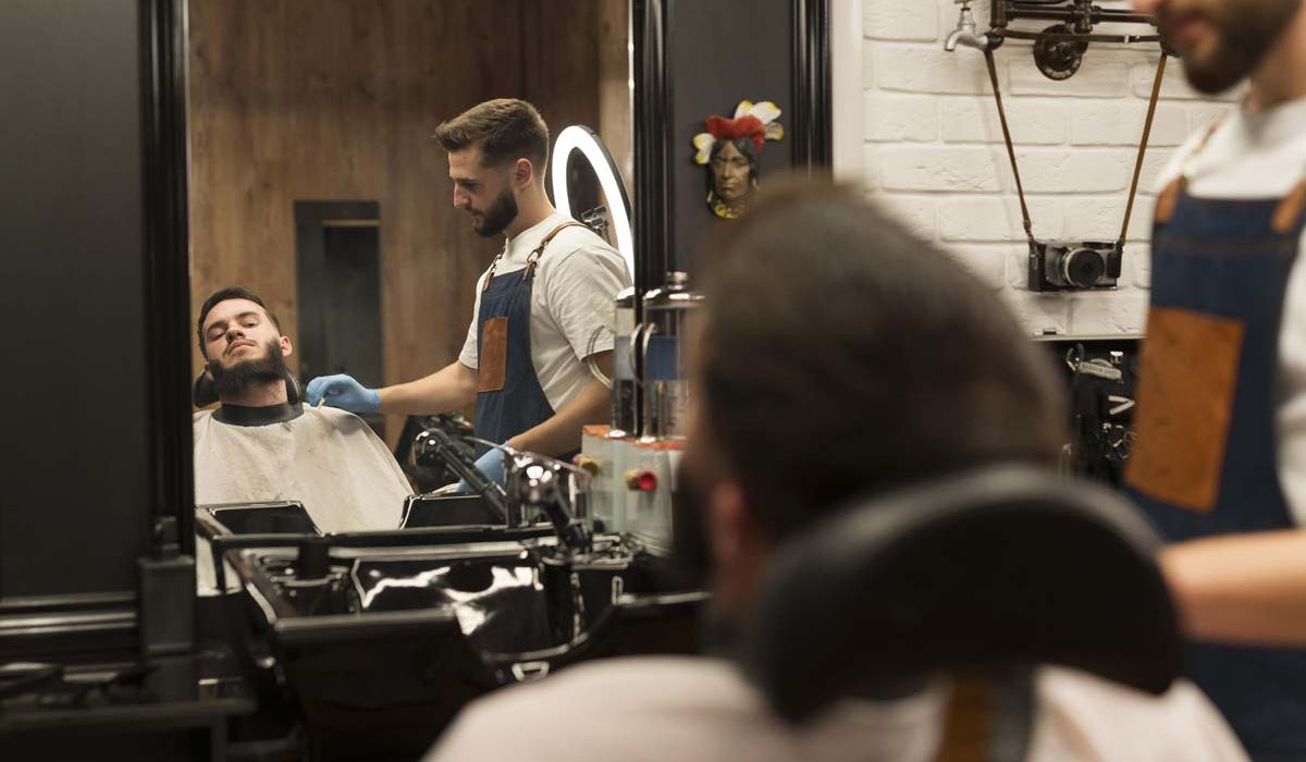 A man receives a haircut from a barber in a well-lit barber shop, surrounded by various hair products and tools.