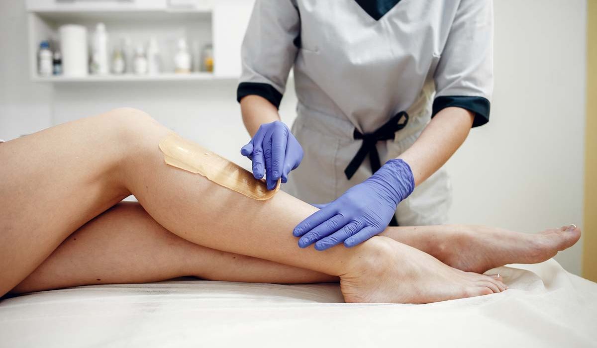 A woman lies on a treatment table while receiving a leg waxing service at a beauty salon.