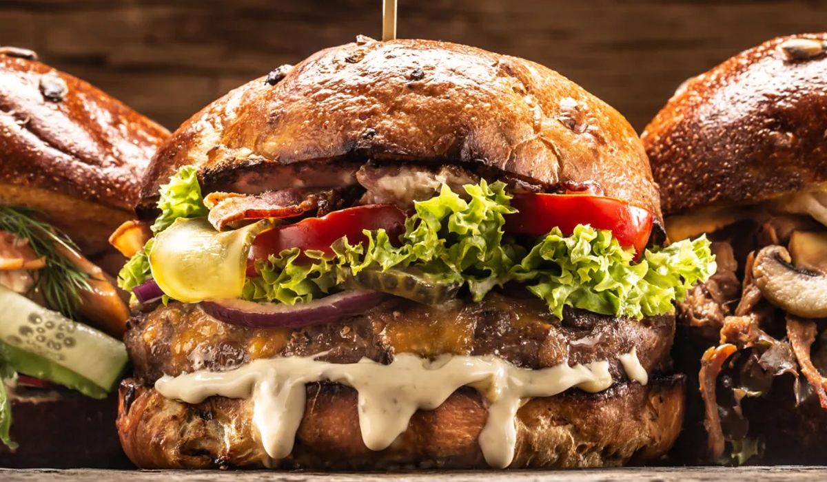 Three types of burgers arranged on a wooden table, highlighting their diverse toppings and flavors.