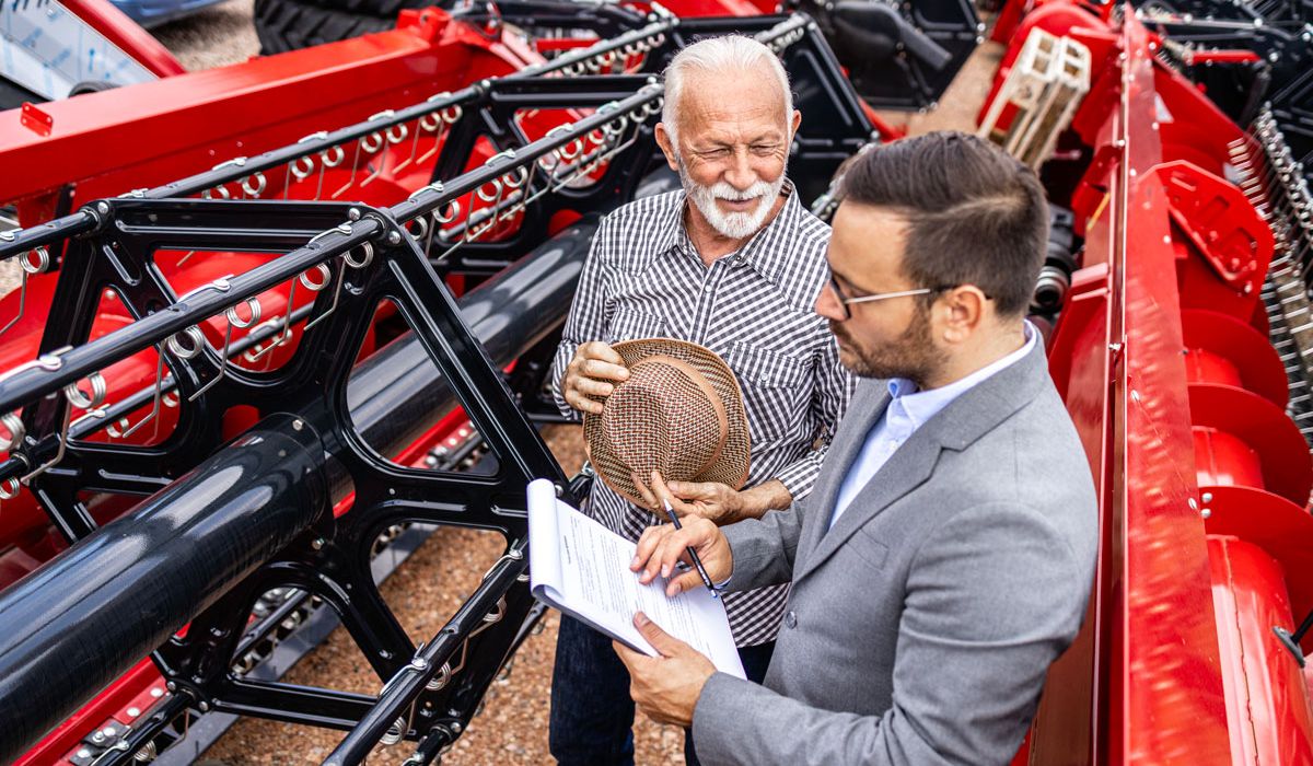 Two men dressed in formal suits pose next to a large tractor