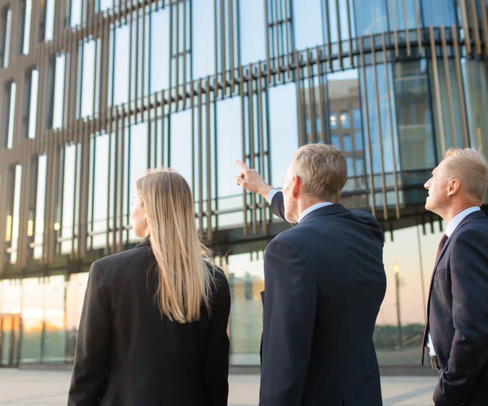 Group of business partners in formal suits pointing at office building